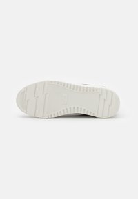 White sneaker sole with ribbed texture, featuring a flat base and vertical grooves for grip. Minimal branding on the heel.
