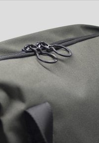 Grijze stoffen tas met een gladde textuur, voorzien van een dubbele ritssluiting met zwarte, ronde trekkerstokken en versterkte stiksels.