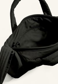 Svart tygväska med två handtag, med en slät yta och dragkedjestängning. Insidan är fodrad med matchande svart material.