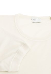 Camicetta beige chiaro a maniche corte realizzata in morbido tessuto, con scollatura rotonda e cuciture rifinite lungo i bordi. Etichetta visibile vicino alla scollatura.