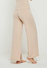 Beige weitgeschnittene Hosen aus weichem Strickstoff mit seitlichen Schlitzen am Saum für zusätzlichen Bewegungsfreiraum und einer lockeren Passform.