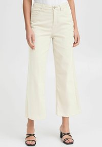 Light beige wide-leg jeans made from denim, featuring a high waist, five pockets, and frayed hems, styled with black strappy heels.