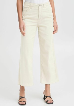 Light beige wide-leg jeans made from denim, featuring a high waist, five pockets, and frayed hems, styled with black strappy heels.