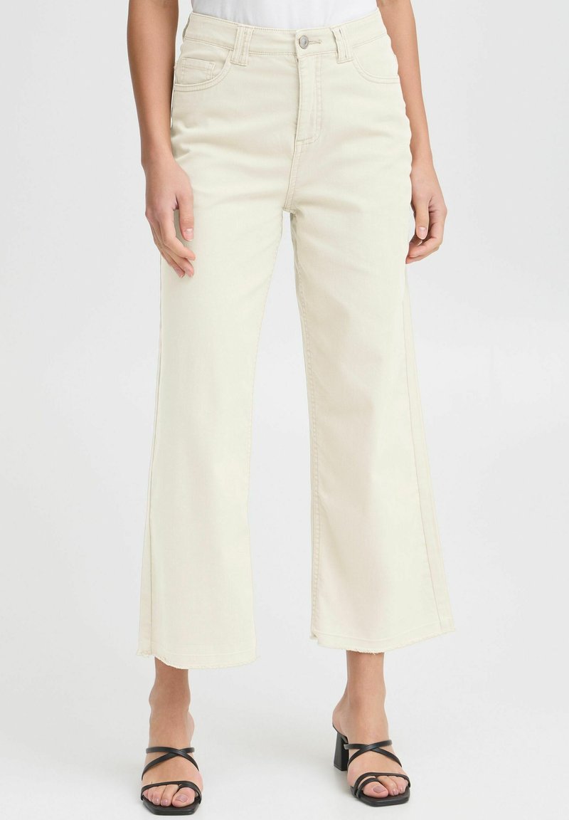 Light beige wide-leg jeans made from denim, featuring a high waist, five pockets, and frayed hems, styled with black strappy heels.