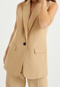 Beige ärmlös blazer i slätt tyg, med slagkrage, en enda knappstängning och två framfickor.