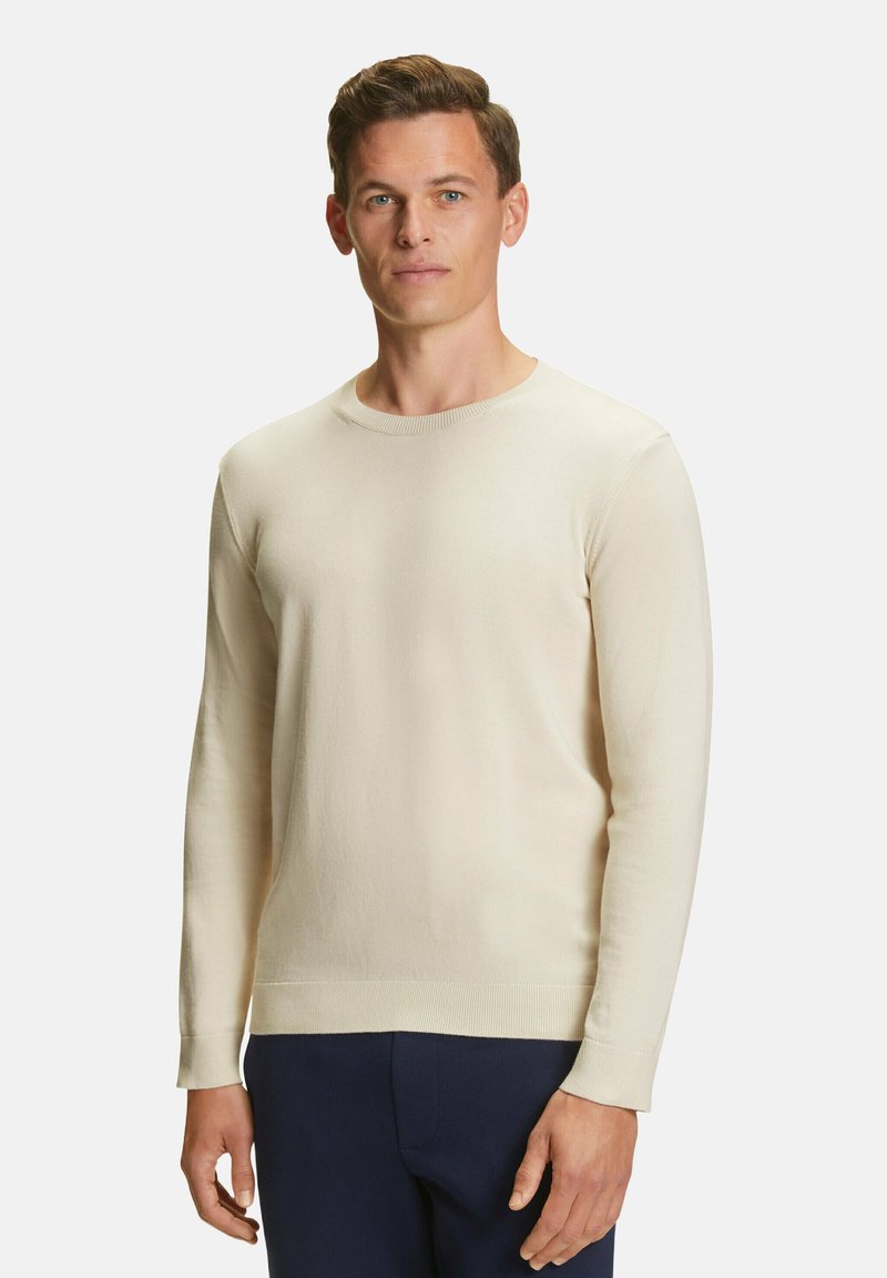 Maglione crew-neck beige chiaro con maniche lunghe, texture liscia, collo e orlo a costine. Indossato con pantaloni blu scuro.