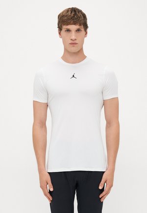 Mand iført en tætsiddende hvid t-shirt med sort Jumpman-logo på brystet, står mod en ensfarvet hvid baggrund.