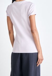 Ljuslila kortärmad topp med ribbad textur, rundad halsringning och figurnära silhuett, bärs med mörka, flödande byxor.