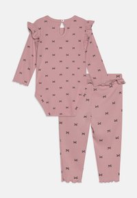 Rózsaszín csíkos bodysuit és nadrág szett fekete masni mintával. Ráncolt ujjakkal, hullámos lábvégekkel és hátsó gombos záródással rendelkezik.