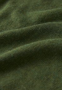 Tessuto di maglia verde con una texture morbida, caratterizzato da sottili variazioni di tonalità e una superficie liscia, leggermente elastica.