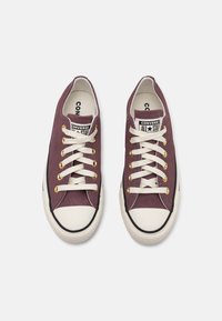 Lilla kanva spordijalatsid valgete kummitaldadega, kreemikad paelad ja kuldsed silmad; musta varbaga ja "Converse All Star" logoga.
