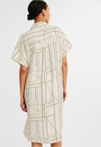 Sukienka z krótkim rękawem w jasnobeżowym kolorze z geometrycznym wzorem w ciemnych liniach, w luźnym kroju i z kołnierzykiem typu shirt.