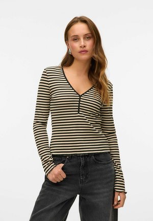 Haut à manches longues rayé avec un décolleté en V, présentant des rayures horizontales noires et beiges et une texture côtelée. Associé à un jean noir taille haute.