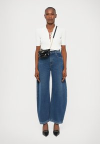 Top alb cu maneci scurte, detaliu cu șnur, pantaloni largi din denim albastru și tocuri negre din piele lactată. Posetă mică neagră cu curea din lanț.