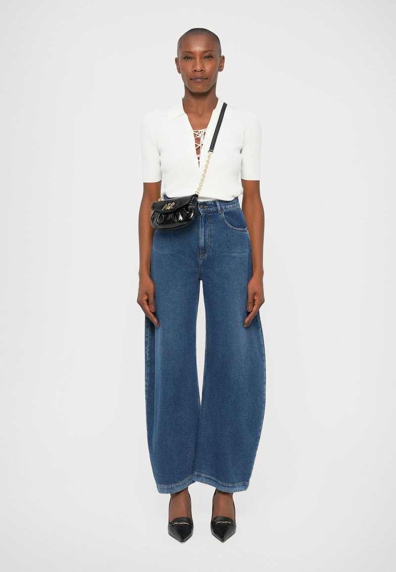 Top alb cu maneci scurte, detaliu cu șnur, pantaloni largi din denim albastru și tocuri negre din piele lactată. Posetă mică neagră cu curea din lanț.