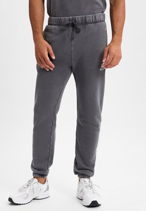 Gray sweatpants with an elastic waistband and drawstring. Cuffed ankles and a small logo on the left side. Worn with white athletic shoes.