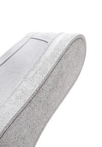 Zapato sin cordones de ante gris con suela de goma blanca texturizada. La parte superior presenta una costura mínima y un acabado suave.