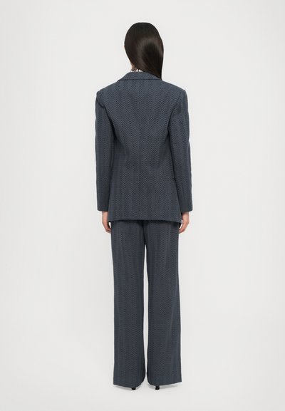 Abbigliamento navy a motivo con una trama a spina di pesce. Presenta un lungo blazer e pantaloni a gamba larga. Vestibilità su misura, dettagli minimi e spalle strutturate.