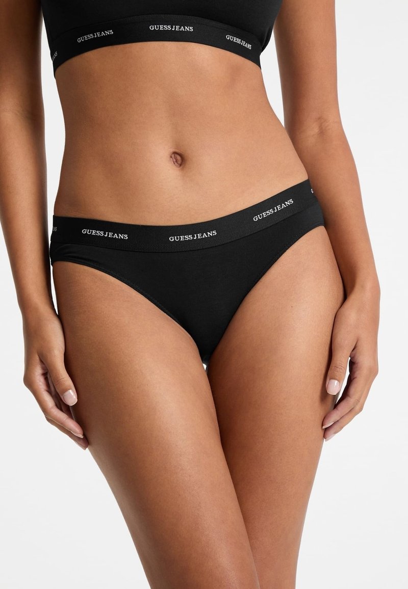 Crni pamukasti bikini s širokim elastičnim pojasom na kojem je u bijelom ispisan tekst "GUESS JEANS". Glatka tekstura, klasičan oblik i minimalistički dizajn.