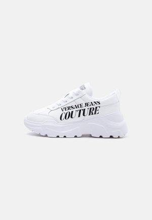 Λευκό chunky sneaker με χοντρή σόλα, σχέδιο με κορδόνια, και την ένδειξη "Versace Jeans Couture" τυπωμένη με έντονα μαύρα γράμματα στο πλάι.