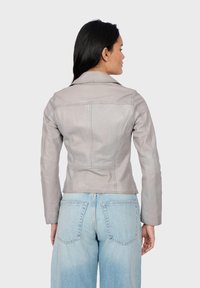 Giubbotto in pelle grigia dal taglio slim, con colletto a revers e dettagli di cucitura visibili. Abbinato a jeans a vita alta di colore blu chiaro.