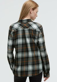 Kariertes Flanellhemd in Schwarz, Weiß und Orange. Mit klassischem Kragen, langen Ärmeln und einer lockeren Passform im Karomuster.