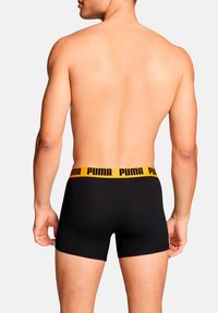 Schwarze Boxershorts mit einem leuchtend gelben Bund, der das Puma-Logo zeigt. Das Design ist glatt und körpernah, hergestellt aus weichem Stoff.