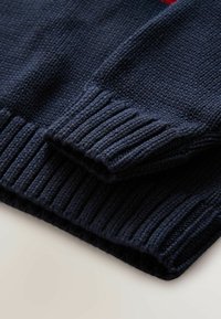 Granatowy sweter z dzianiny z prążkowanymi mankietami i dołem, charakteryzujący się teksturowanym materiałem oraz zbliżeniem na detale rękawów.