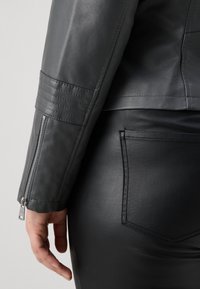 Μαύρο μπουφάν από τεχνητό δέρμα με φερμουάρ στους μανικιών, διαθέτει ραμμένες λεπτομέρειες στα μανίκια και σχεδίαση slim-fit. Λείο υφή και εφαρμοστό σχήμα.