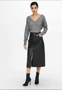 Sivi pleteni pulover z V-izrezom, kombiniran s črno usnjeno midi krilo s sprednjim razporkom in črnimi gležnjaki.