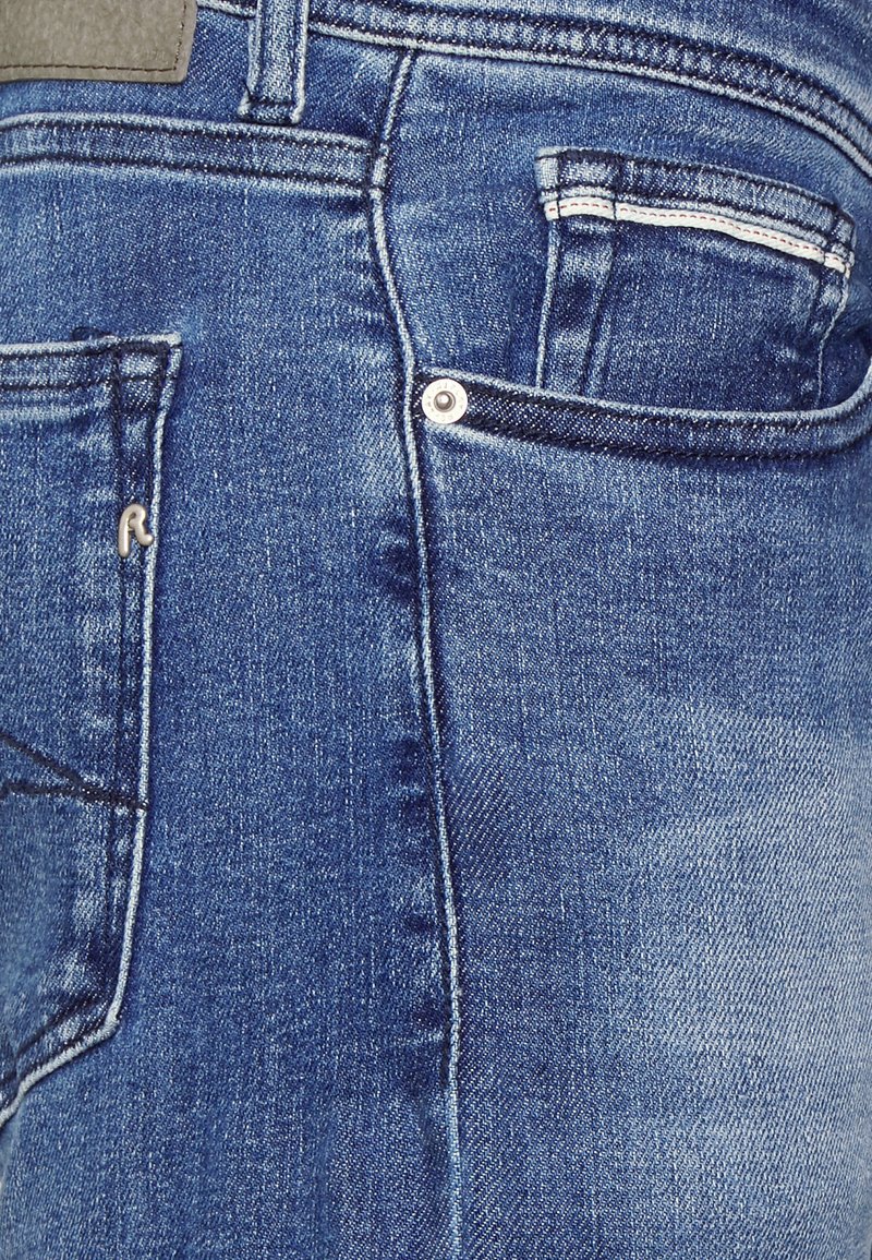 Dunkelblaue Denim-Jeans mit einer Gesäßtasche, silbernem Niet und Stickdetails. Strukturiertes Material mit einem leicht ausgewaschenen Effekt.