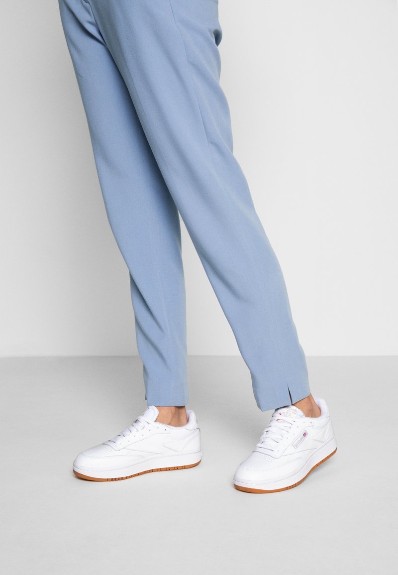 Vita sneakers med gummisula och varumärkesdetaljer, i kombination med ljusblå, plisserade, skräddarsydda byxor med avsmalnande ben och ankelslitsar.