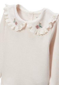 Vêtement en tissu côtelé blanc avec un col festonné orné de broderies florales roses et vertes. Détail de fermeture à boutons à l'arrière visible.