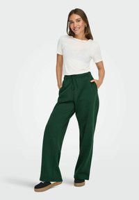 Grønne brede sweatpants med elastisk talje og lommer, parret med en hvid t-shirt. Outfitet har en afslappet og komfortabel pasform.