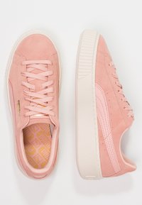 Baskets en daim roses avec des semelles en caoutchouc blanches épaisses, des lacets et une bande latérale rose, présentées en vues de dessus et de côté sur un fond blanc.