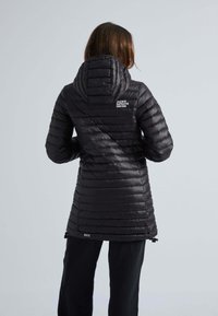 Svart, isolerad lång jacka med vertikala quiltade mönster, justerbar huva och logotyp på övre delen av ryggen. Har dragsnören i nederkant.