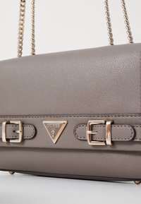 Borsa grigia con texture e hardware dorato, tra cui un logo triangolare e fibbie. Presenta una tracolla a catena per il trasporto.