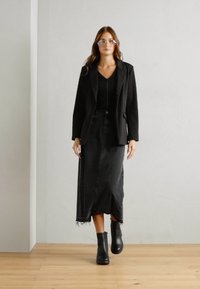 Svart blazer over en svart topp, kombinert med et høyt liv svart denim skjørt med en frynset kant. Svart ankelstøvletter fullfører antrekket.