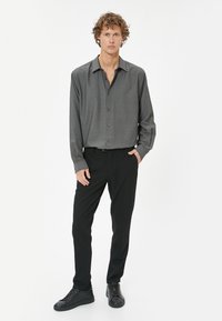 Chemise à manches longues grise à boutons avec une texture subtile, associée à un pantalon noir et des baskets noires à lacets, présentant un col standard.