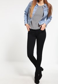 Chaqueta de mezclilla en azul claro, top a rayas en blanco y negro, jeans skinny negros y botines negros. Textura suave y diseño entallado.