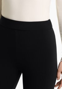 Fekete leggings magas derékkal, sima textúrával és testhez simuló fazonnal, semleges háttér előtt bemutatva.