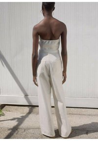 Pantalon ample de couleur crème avec poches avant, associé à un haut simple sans bretelles. Texture lisse et coupe décontractée, sur fond atténué.