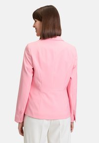 Lichtroze aansluitende blazer met gestructureerde schouders, knoopmanchetten en een soepele textuur. De achteraanzicht benadrukt de op maat gemaakte naden en strakke lijnen.
