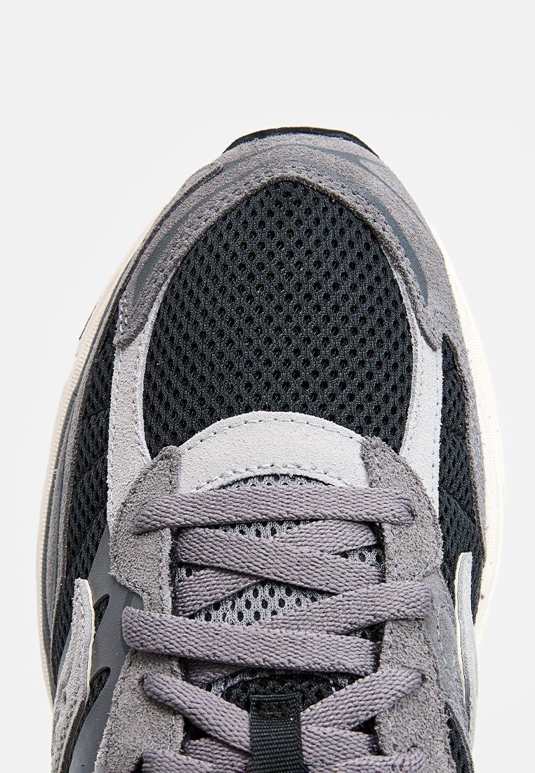 Gros plan sur une sneaker de sport grise et noire avec une tige en mesh et de grosses lacets gris noués en motif croisé.