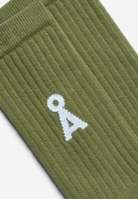 Olivgrüne, gerippte Socken aus weichem Stoff mit einem weißen, gestickten Buchstaben "A" als Logo. Klassisches Design in Crew-Länge.