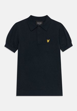 Μαύρο κοντομάνικο πόλο με γιακά, πατιλέτα με κουμπιά και μικρό κίτρινο λογότυπο αετού στο αριστερό στήθος.