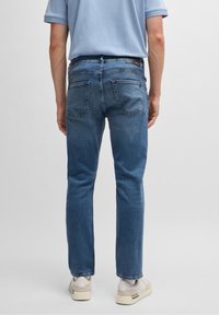 Světle modré džínové kalhoty s rovnými nohavicemi, zadními kapsami, jemnými švy, opotřebovaným vzhledem, spárované s béžovými teniskami.