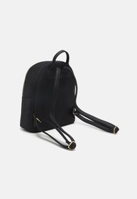 Black backpack with a smooth fabric exterior, rounded shape, dual shoulder straps, and a zip closure. Features gold-tone accents.