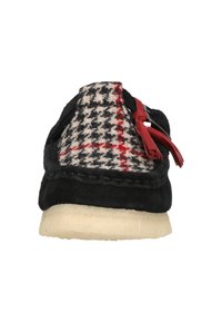 Zwarte suède pantoffel met een houndstooth bovenwerk in zwart, wit en rood, met rode accenten en een vlakke crèmekleurige zool.