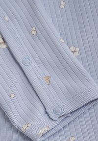 Lichtblauwe ribstof met kleine bloempatronen en een bijpassende knoopsluiting. Zachte textuur met een comfortabele pasvorm.